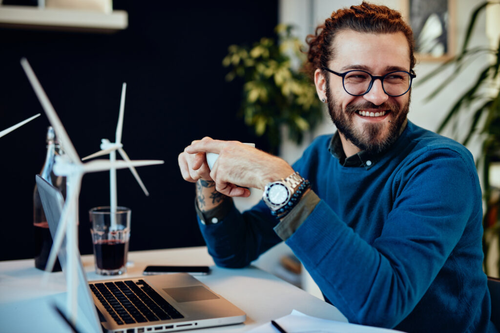 Smiling entrepreneur working at a laptop with wind turbine models and financial templates—accessing free downloadable tools from The William Stanley CFO Group to make smarter business decisions