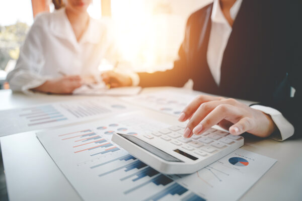 Hands using a calculator over financial charts during a strategy session, reflecting The William Stanley CFO Group's US News feature on maximizing financial benefits.