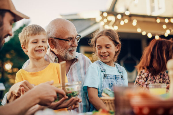 Multigenerational family smiling and sharing food at an outdoor gathering, representing The William Stanley CFO Group’s Go Banking Rates feature on smart financial planning across life stages.