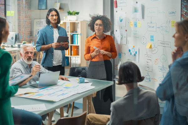 Team of diverse professionals in a collaborative workspace with whiteboards and planning materials, representing The William Stanley CFO Group’s Yahoo Finance feature on the 7-Day Rule.