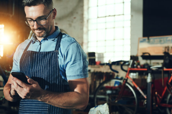 Focused entrepreneur in an apron reviewing financial data on a tablet in a bike shop, representing clarity and trend analysis using a vertical income statement