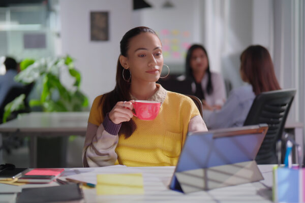 Professional woman sipping coffee while reviewing a tablet in a modern office, reflecting The William Stanley CFO Group’s quote on AI in banking.