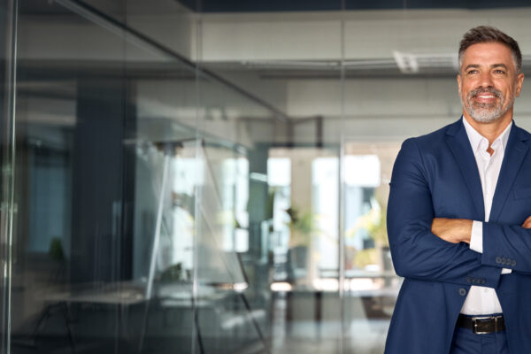 Confident business professional standing in a modern glass office, representing The William Stanley CFO Group’s FlexJobs feature on virtual leadership strategies.
