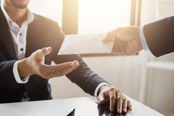 Close-up of a businessperson handing a document across a desk, representing The William Stanley CFO Group’s Think Money feature on quantifying soft savings in business decisions.