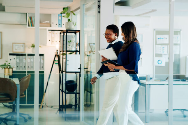 Two professionals smiling and walking through a modern office with glass walls and file shelves, representing The William Stanley CFO Group’s Think Money feature on top financial films.