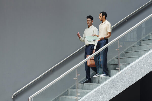 Two professionals walking down a stairwell in conversation, symbolizing The William Stanley CFO Group’s GOBankingRates feature on financial steps after a holiday layoff.