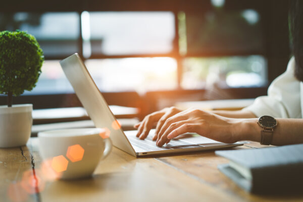 Person typing on a laptop at a sunlit desk, with coffee and notes—reading The William Stanley CFO Group’s business blog for actionable financial insights